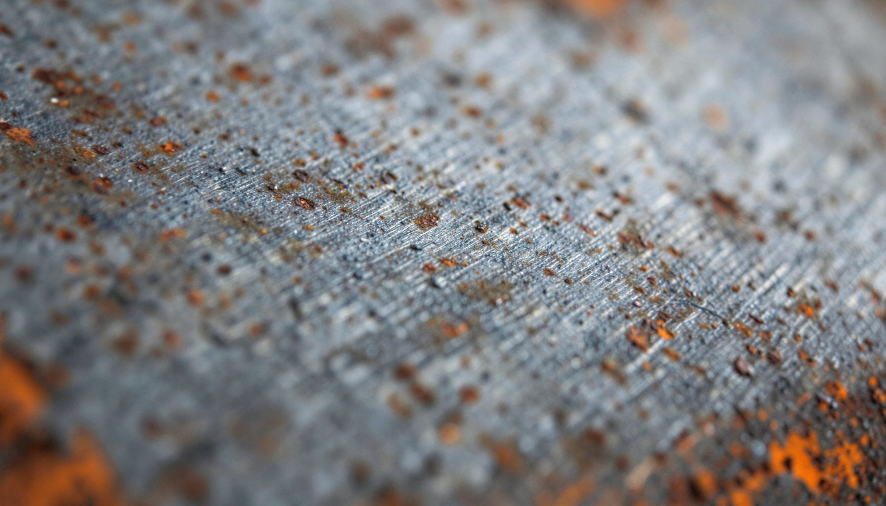 Extreme close-up of weathered brushed metal texture in muted slate gray and charcoal tones with subtle rust highlights, conveying an industrial and timeless mood.