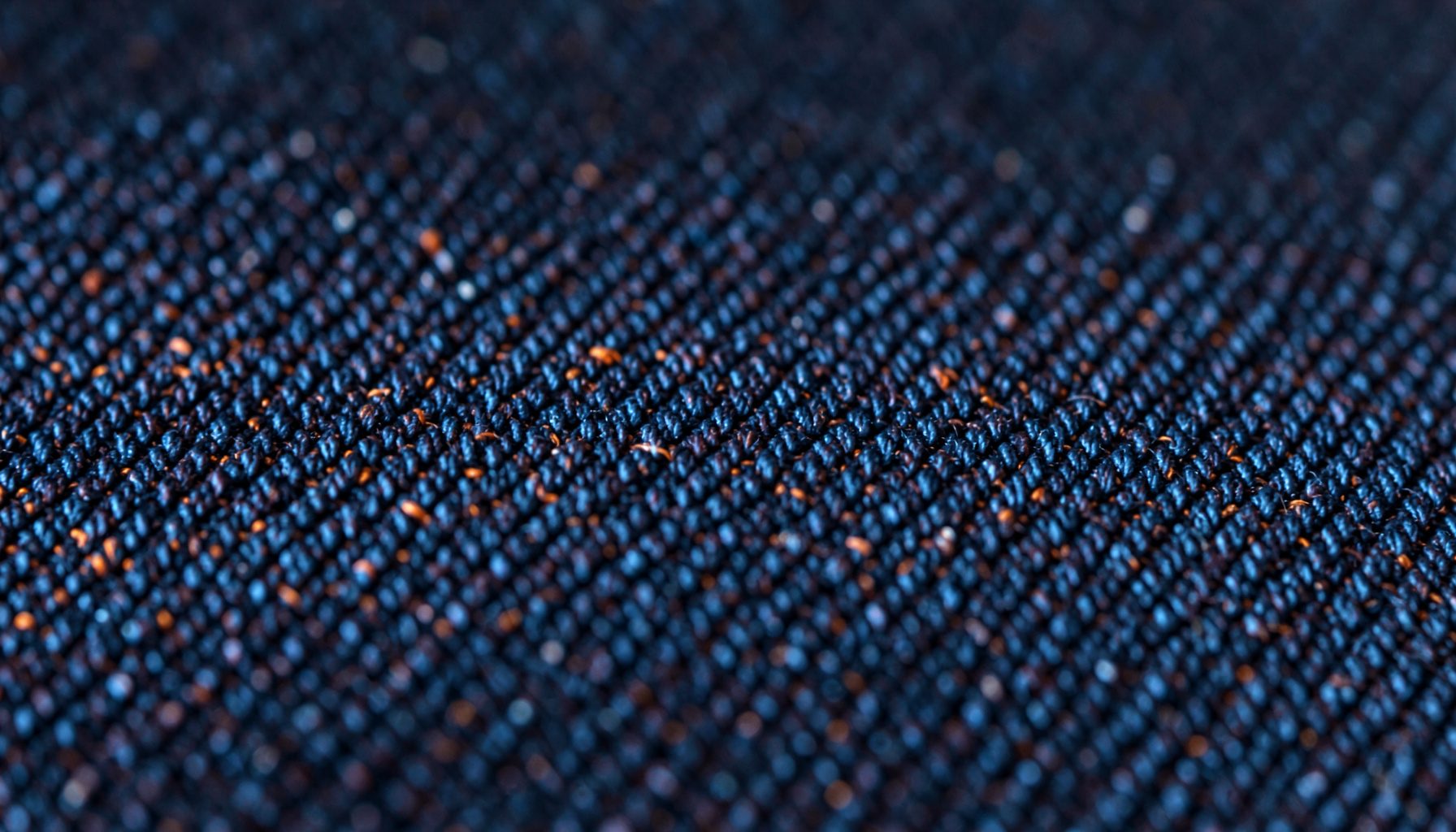 Extreme close-up of dark indigo denim fabric weave with coarse diagonal twill texture and soft navy highlights, calm and understated mood.